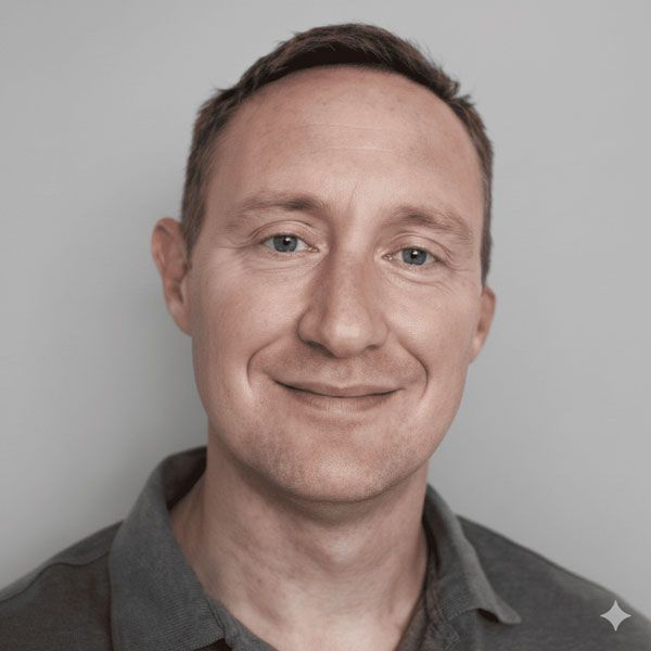 Man with short brown hair, smiling, wearing a gray polo shirt, against a gray background.
