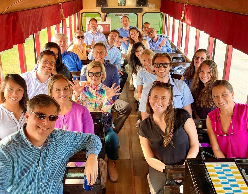 Group of smiling people seated inside a red-canopied trolley, posing together on a sightseeing ride.