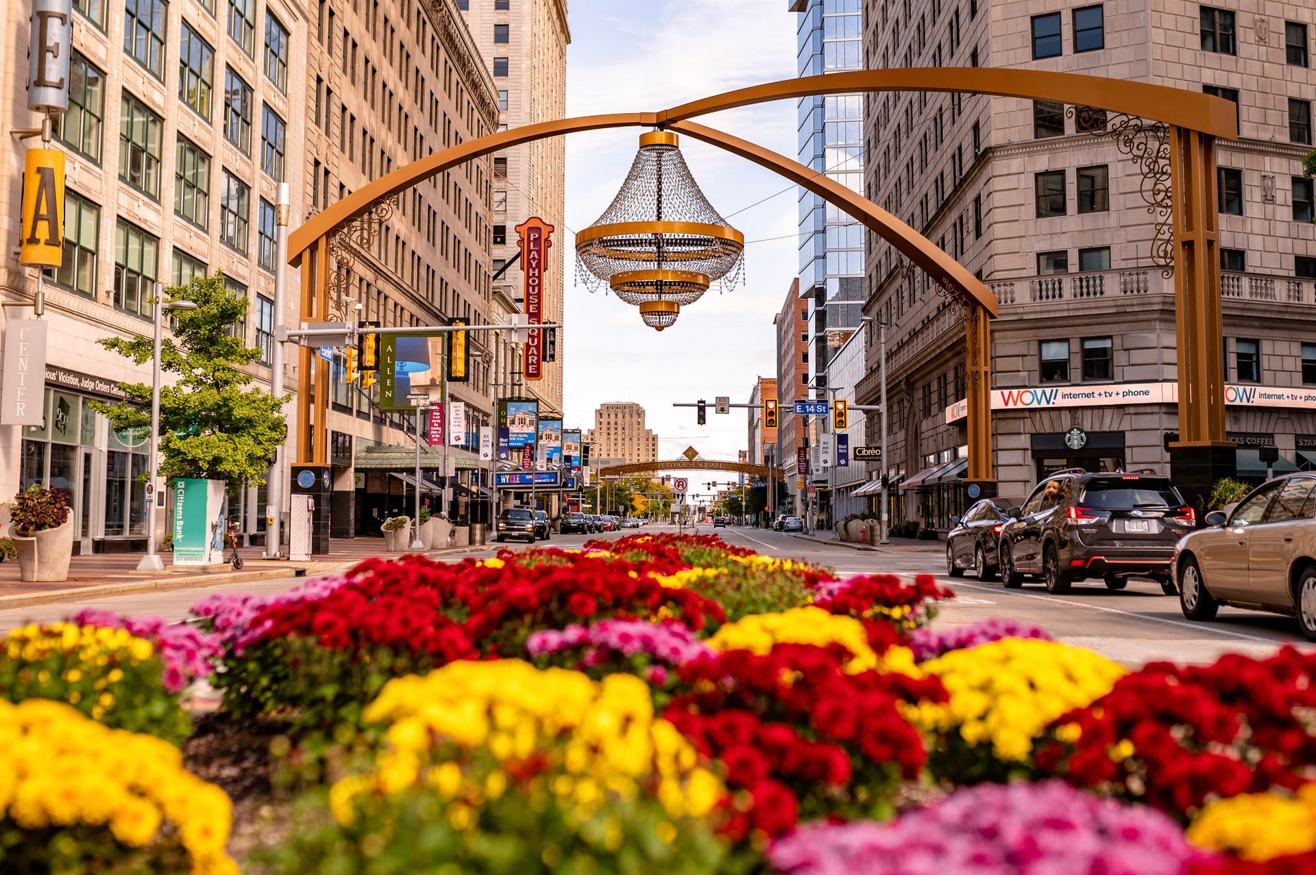 Downtown street with colorful flower beds and a large hanging basket sculpture between buildings