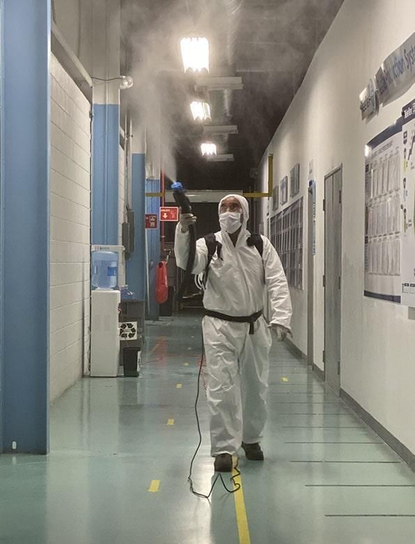 Un hombre con un traje de protección está rociando desinfectante en un pasillo.