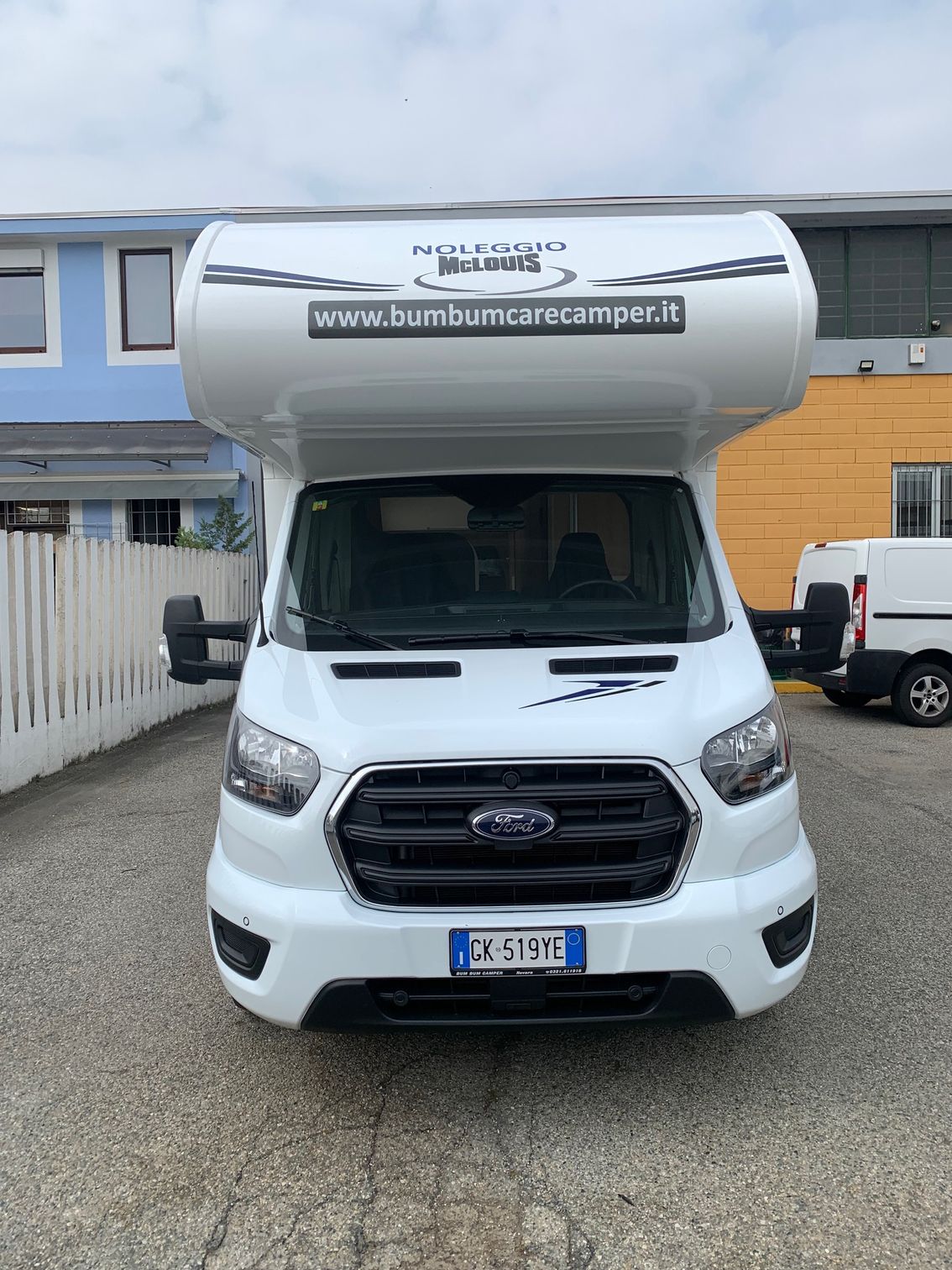 Un camper bianco è parcheggiato nel vialetto di una casa con recinzione.