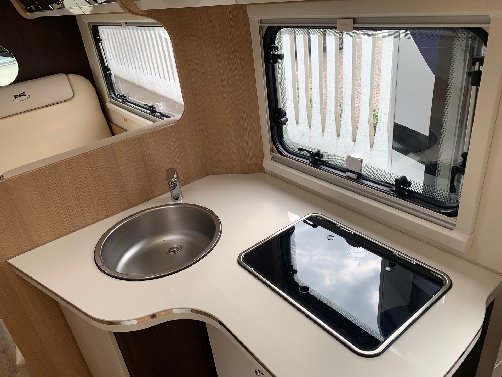 Angolo cottura compatto per camper con lavello in acciaio inox, piano cottura nero e tende alle finestre.