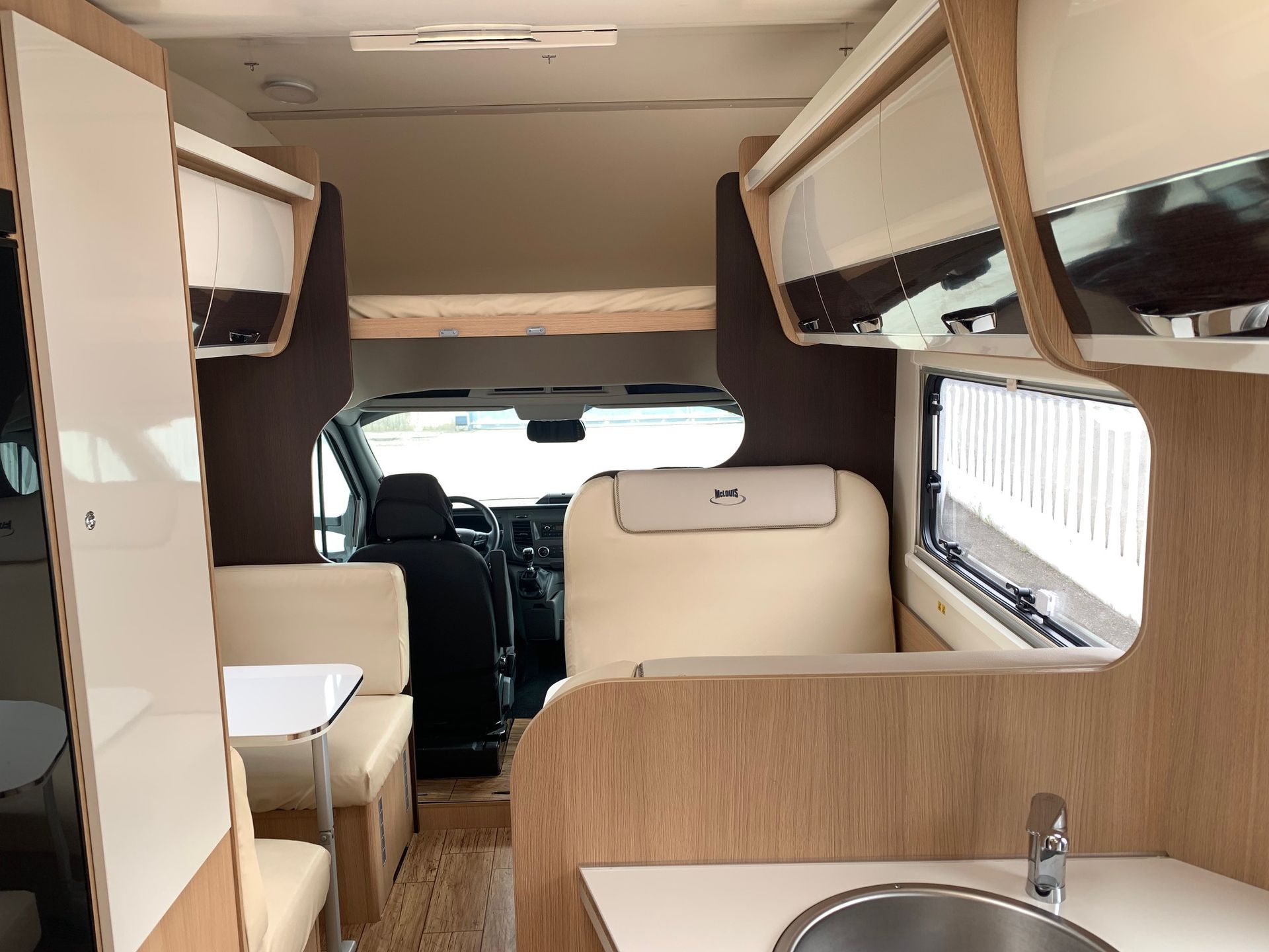 Interno di un camper compatto con mobili in legno, sedile a panca e cabina anteriore visibile.