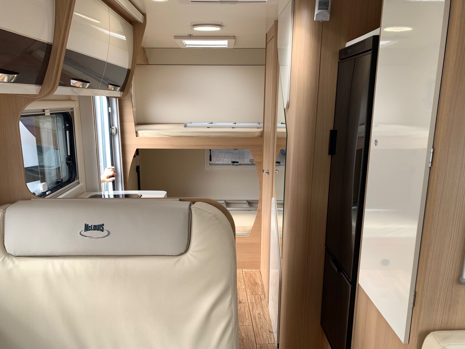 Interno compatto del camper con sedili beige, armadietti in legno e letto a castello nella parte posteriore.