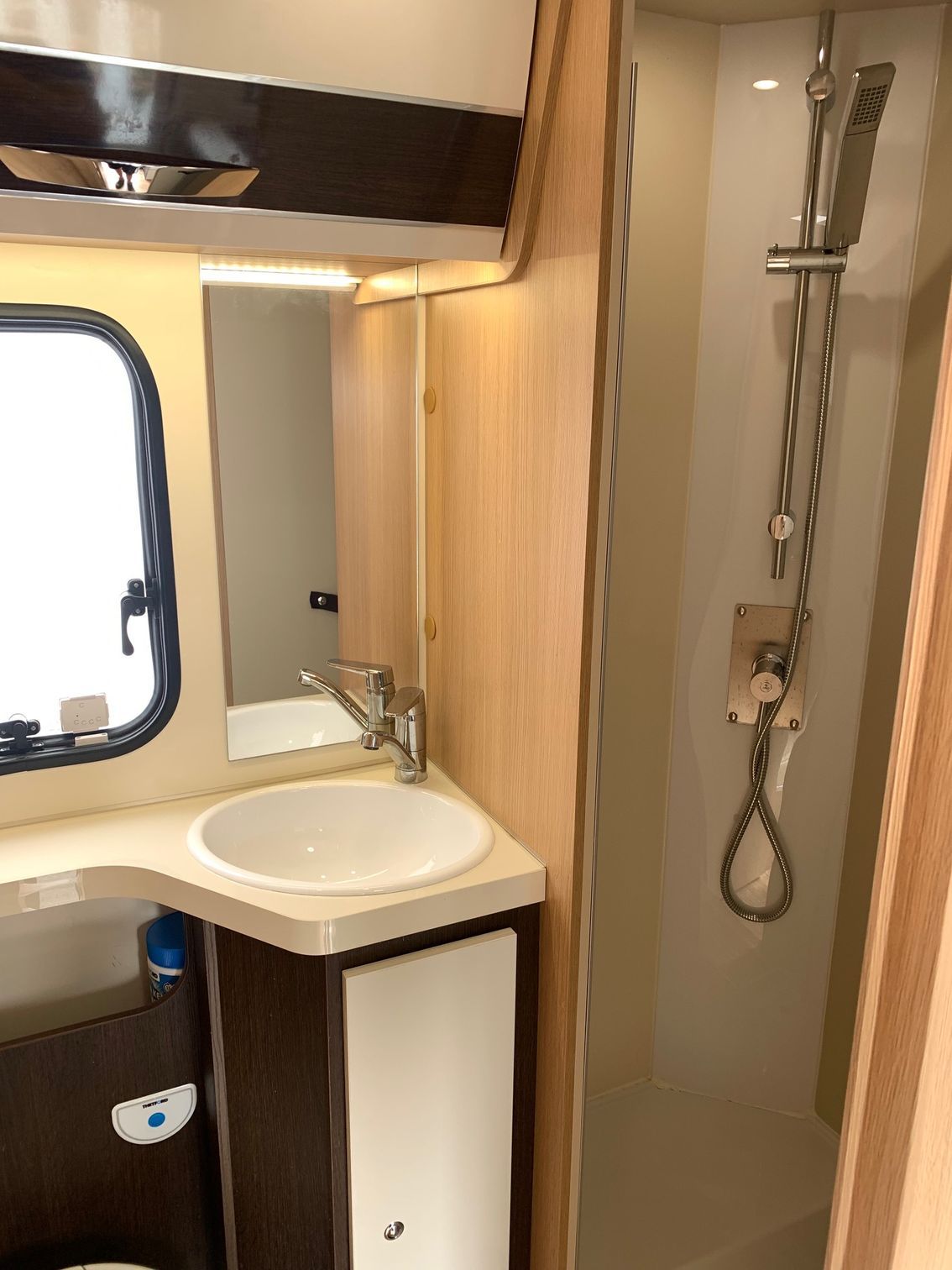 Bagno compatto per camper con lavandino, specchio e box doccia con doccetta a mano.