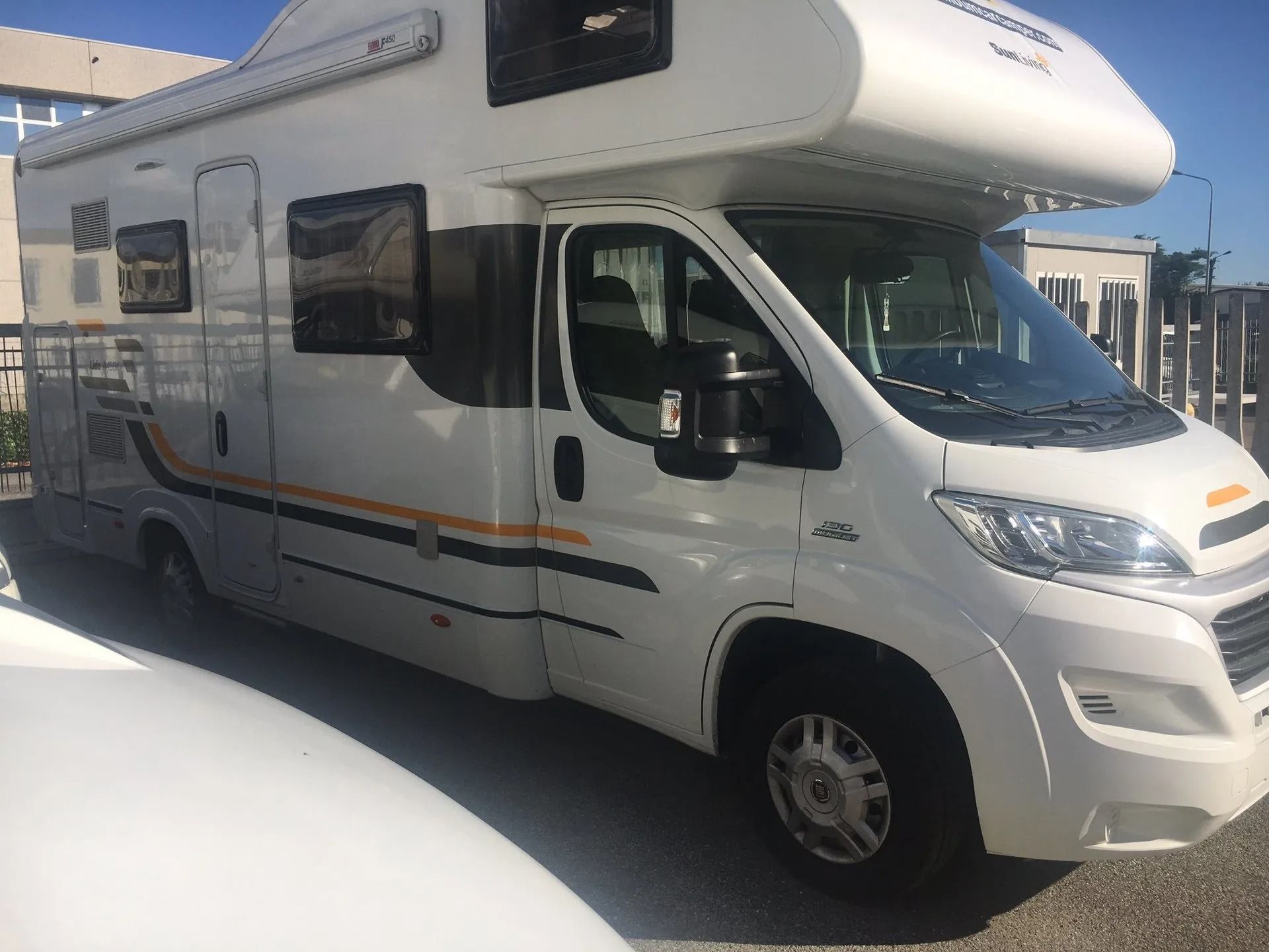 Camper bianco parcheggiato all'aperto in piena luce solare, vista laterale con tetto a soffietto per dormire.