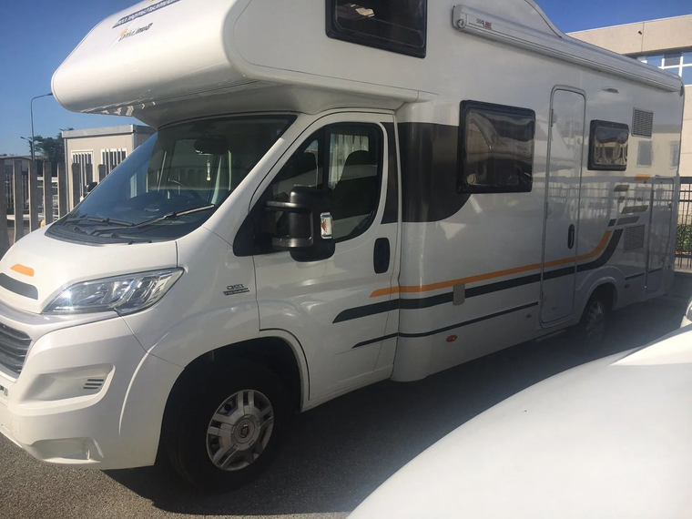 Un camper bianco parcheggiato all'aperto, in pieno sole, con tetto rialzato e finestrini laterali.