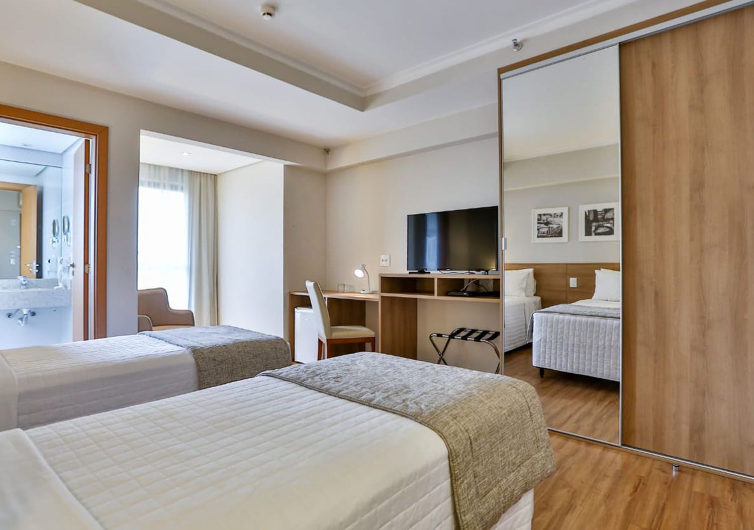 Um quarto de hotel com duas camas, uma escrivaninha, uma televisão e um espelho.
