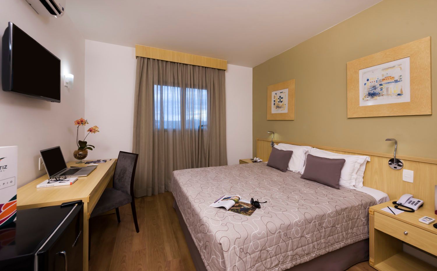 Um quarto de hotel com uma cama king size, escrivaninha, laptop e televisão.