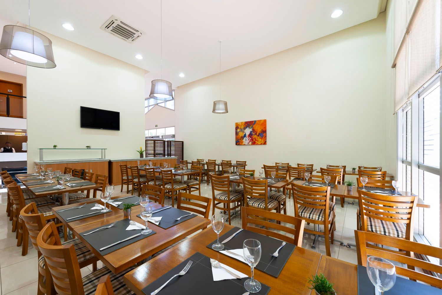 Uma grande sala de jantar com mesas e cadeiras e uma televisão na parede.