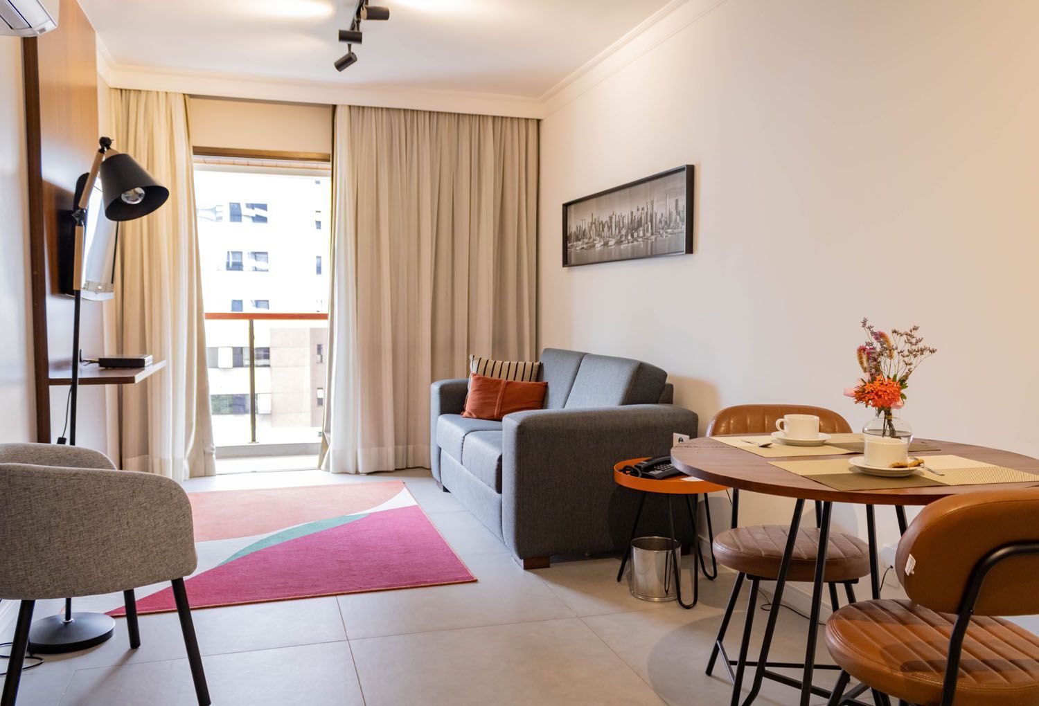 Uma sala de estar com sofá, mesa, cadeiras e uma varanda.
