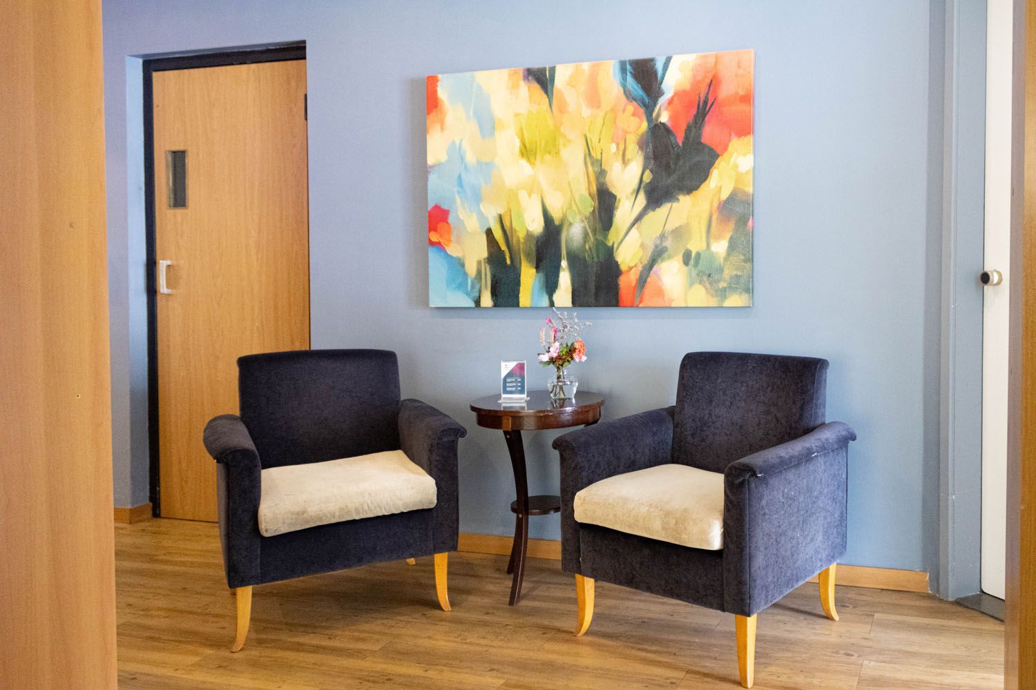 Duas cadeiras e uma mesa em uma sala com uma pintura na parede.