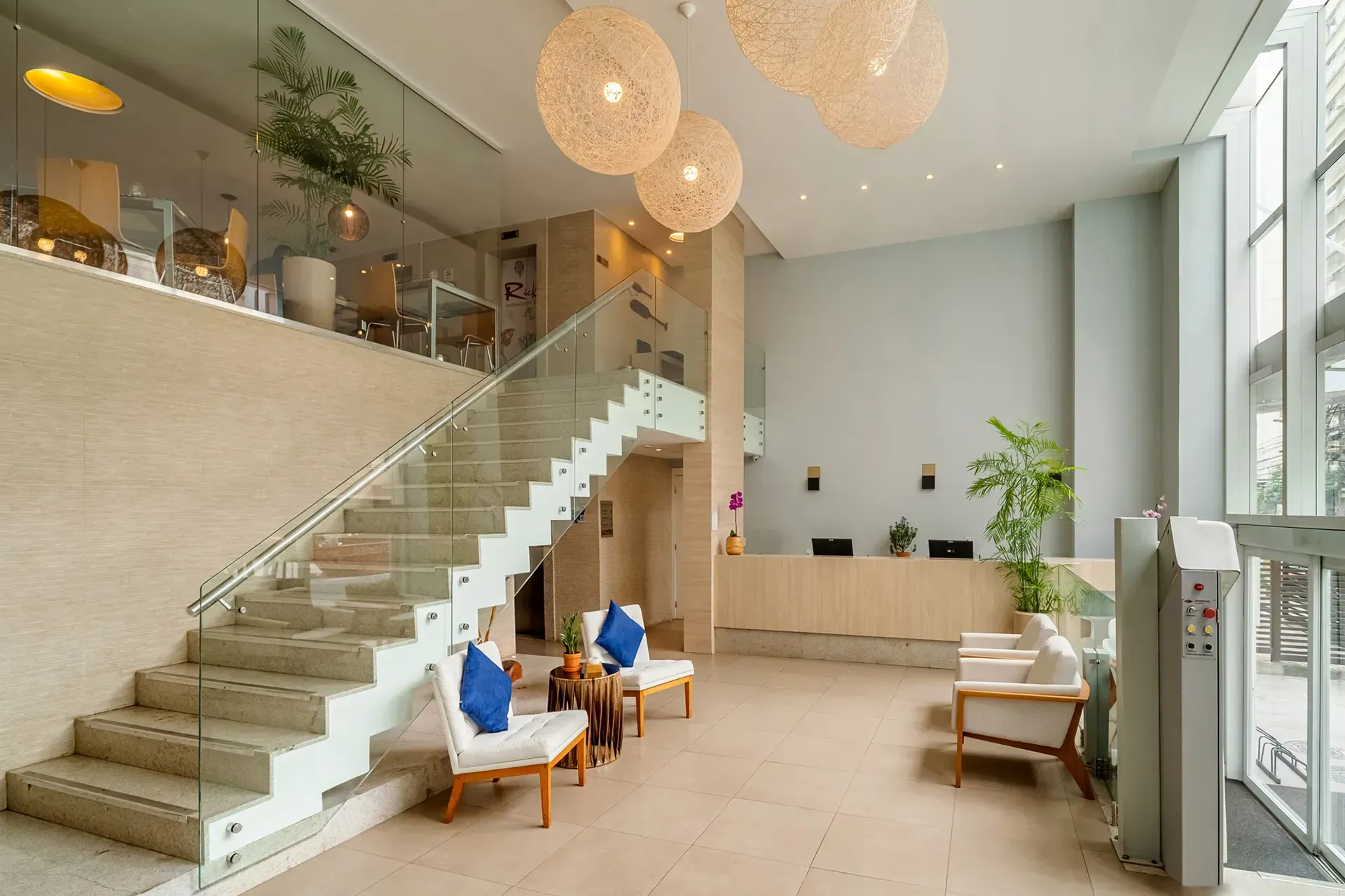 Um lobby de hotel com escadas que levam ao segundo andar e um balcão de recepção.