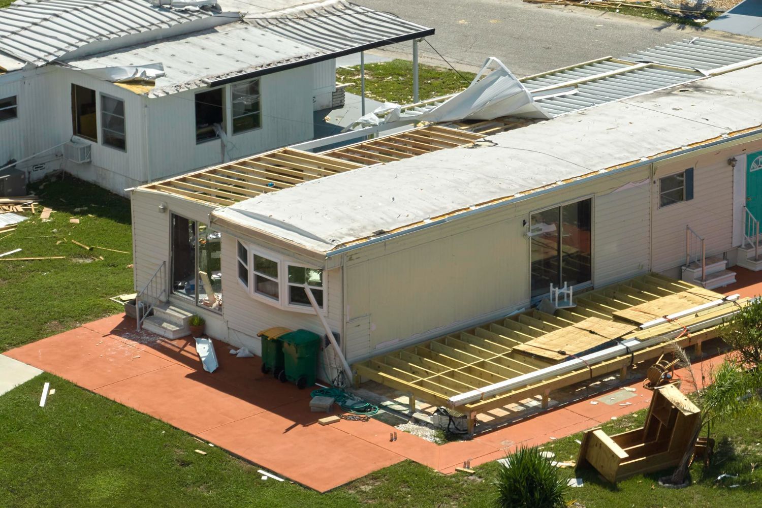 Damaged mobile home; roof and deck partially destroyed. Debris and exposed structure visible.
