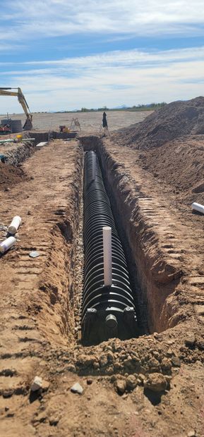 A large pipe is being installed in a trench in the dirt.