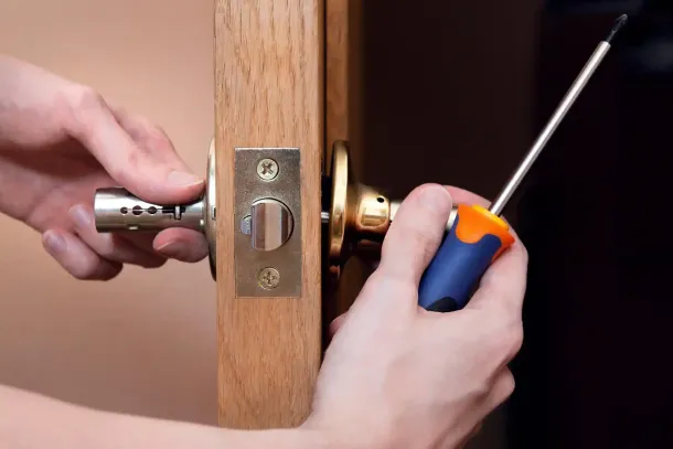 Mani che utilizzano un cacciavite per installare una maniglia su una porta di legno.