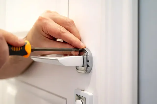 Persona che utilizza un cacciavite per installare o riparare una maniglia cromata su una porta bianca.