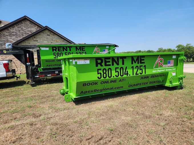 A green dumpster is parked in front of a house.