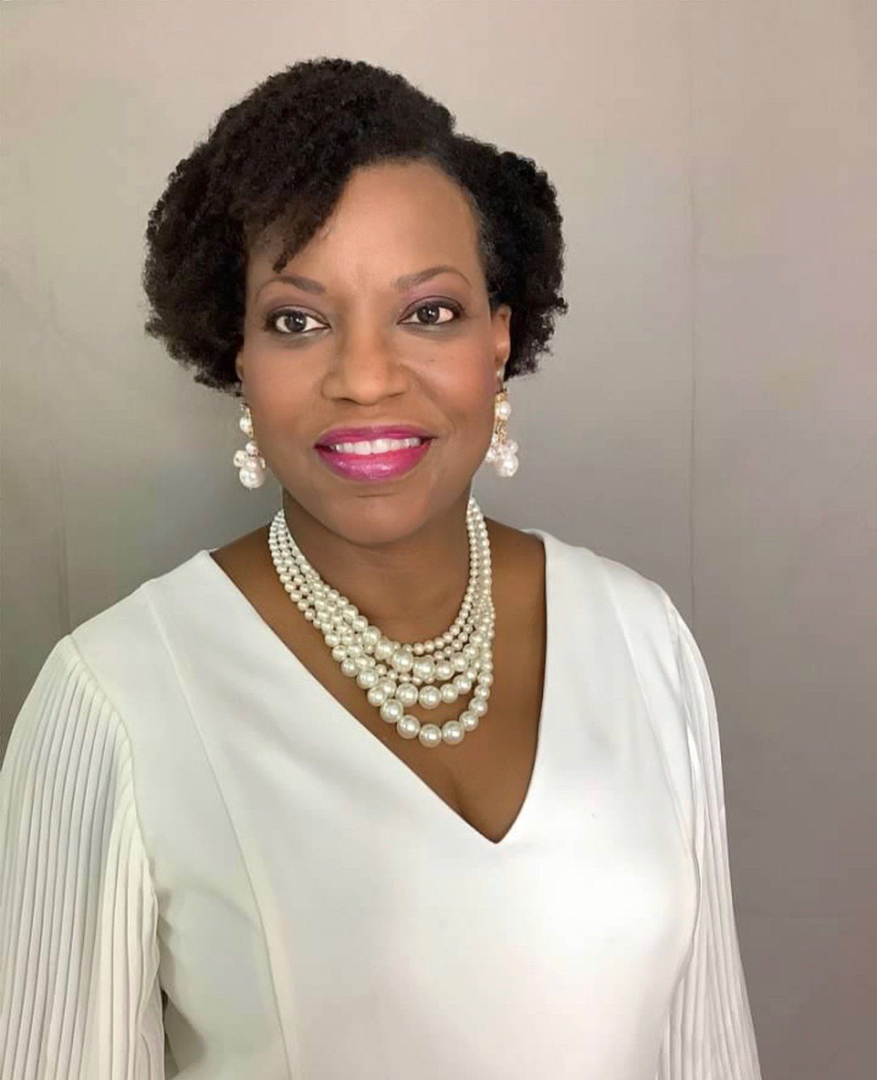 A woman wearing a white dress and pearls is smiling for the camera