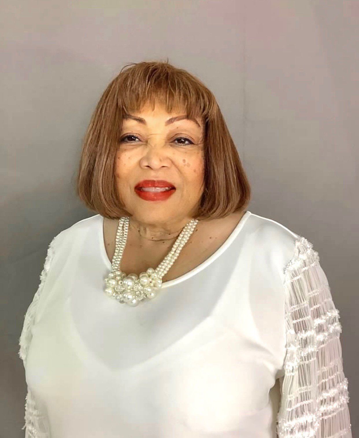The woman is wearing a white shirt and a pearl necklace.