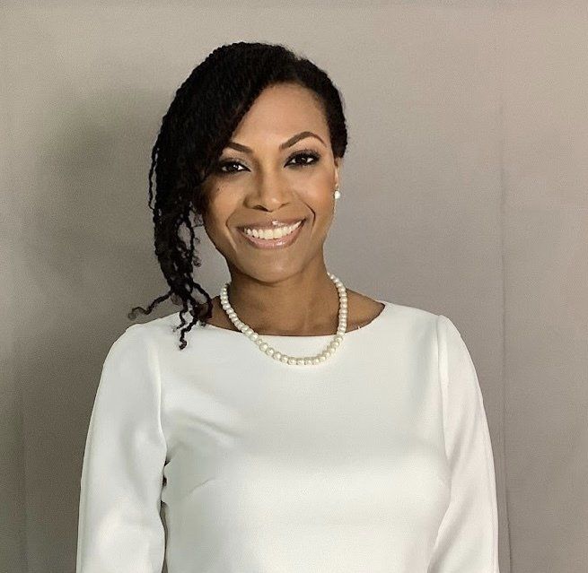 A woman wearing a white shirt and a pearl necklace smiles for the camera.