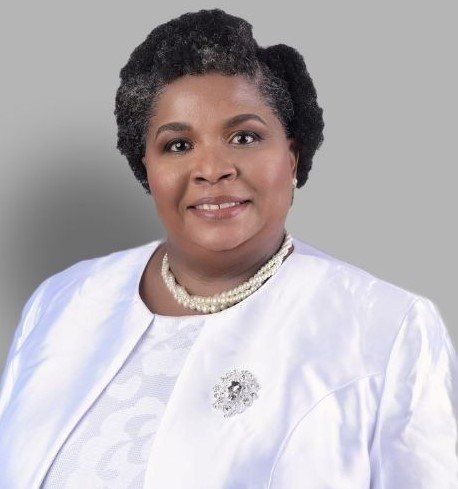 A woman wearing a white jacket and pearls is smiling for the camera.