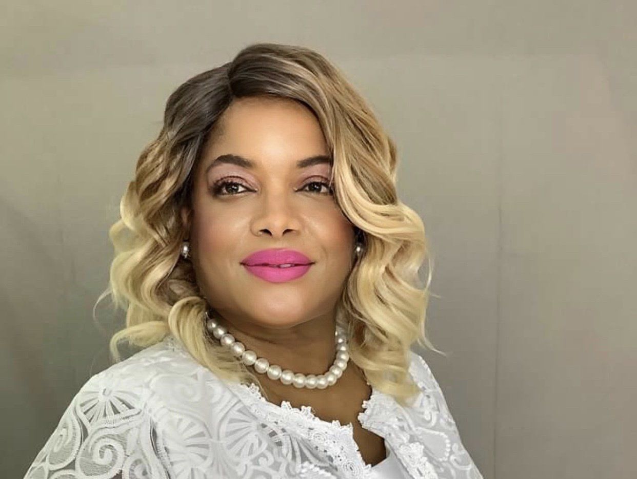 A woman wearing a wig and a pearl necklace is smiling for the camera.