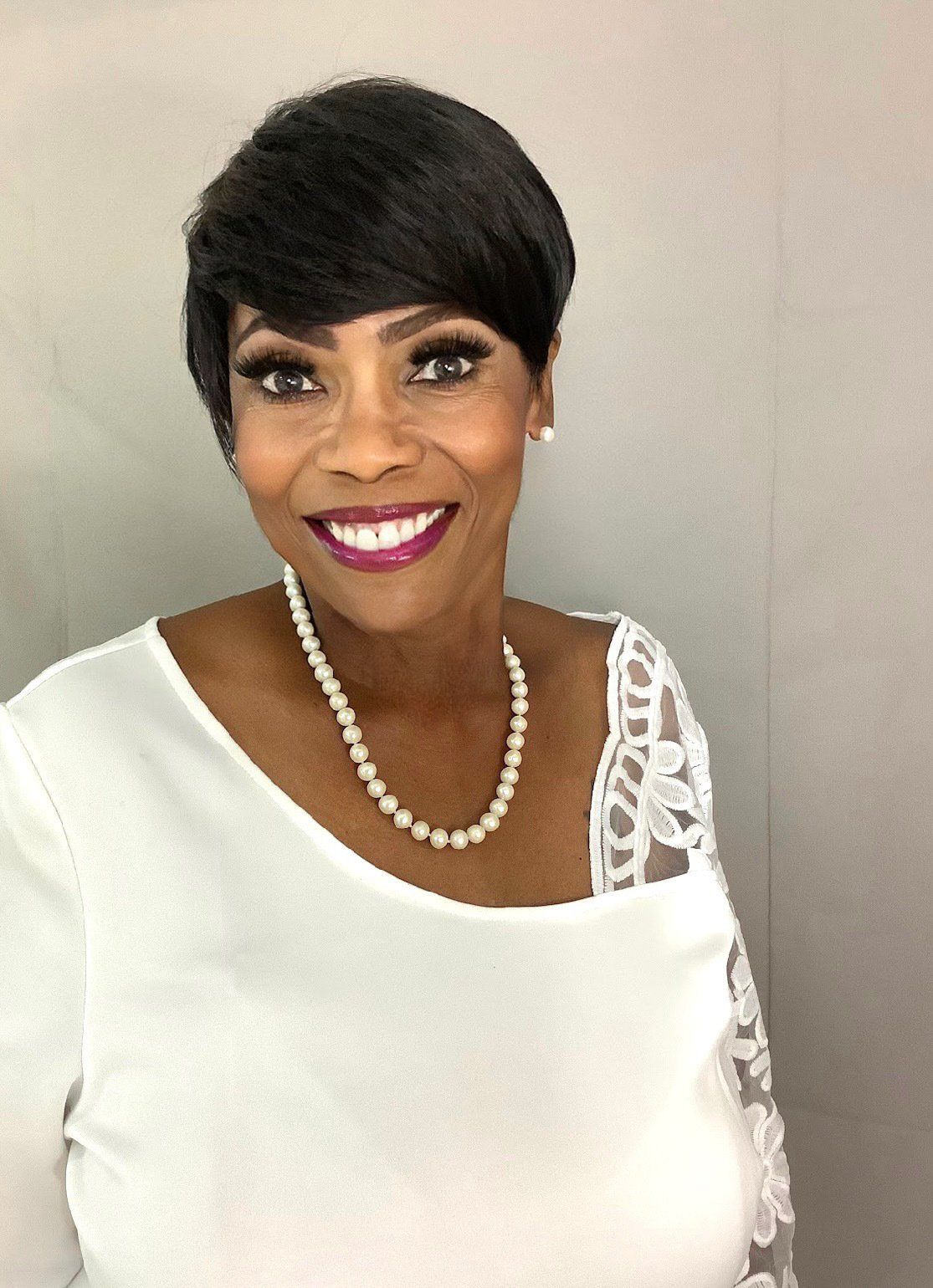 A woman wearing a white shirt and a pearl necklace is smiling for the camera.