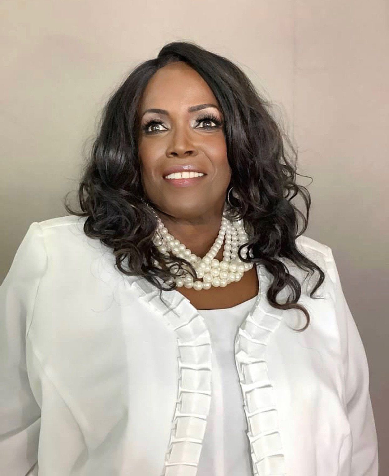 A woman wearing a white jacket and pearls is smiling for the camera.