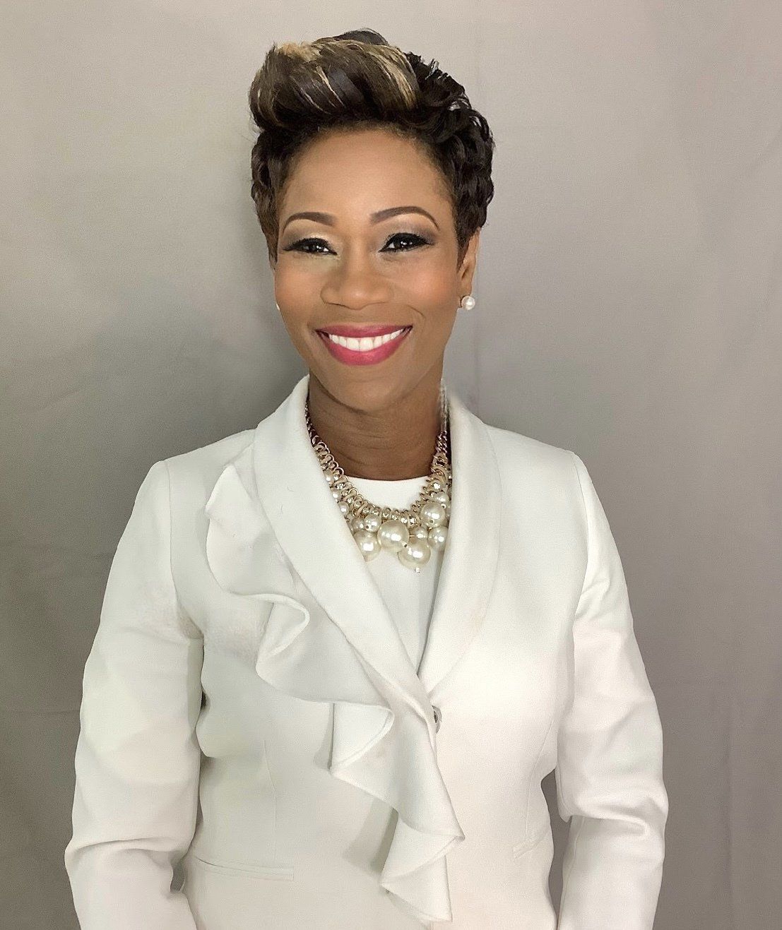 A woman wearing a white jacket and pearl necklace smiles for the camera