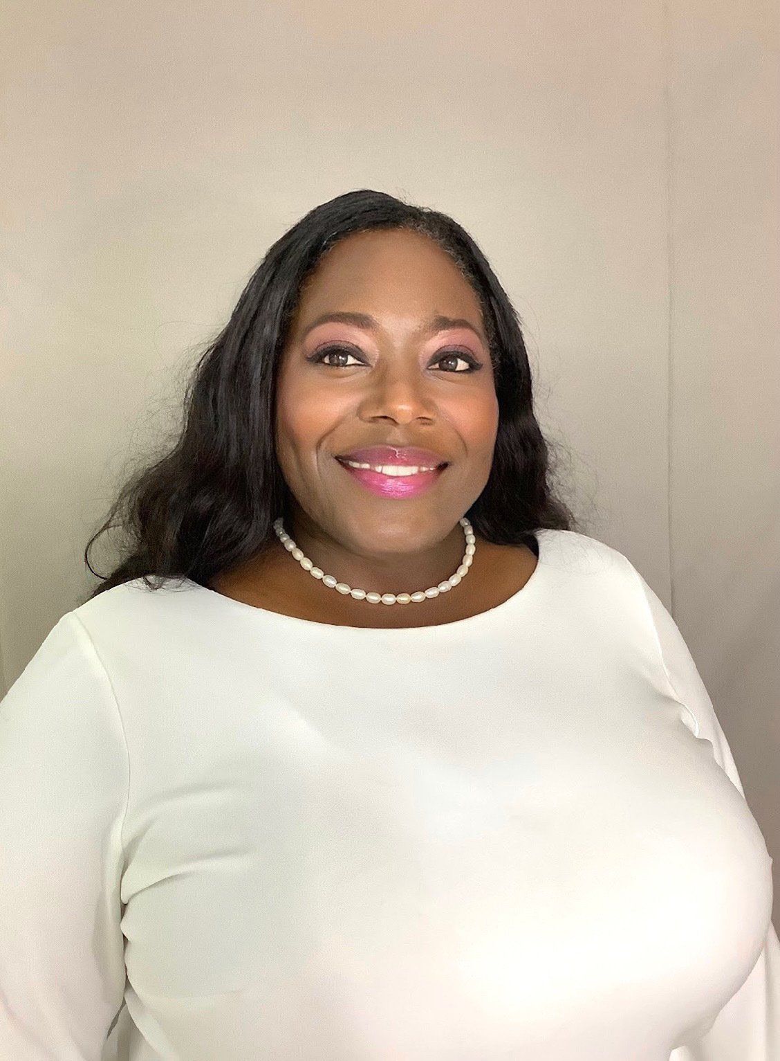 A woman wearing a white shirt and a pearl necklace is smiling for the camera.