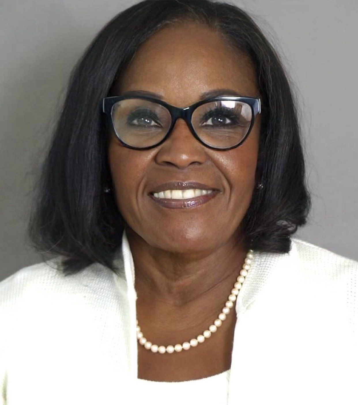 A woman wearing glasses and a pearl necklace is smiling for the camera.
