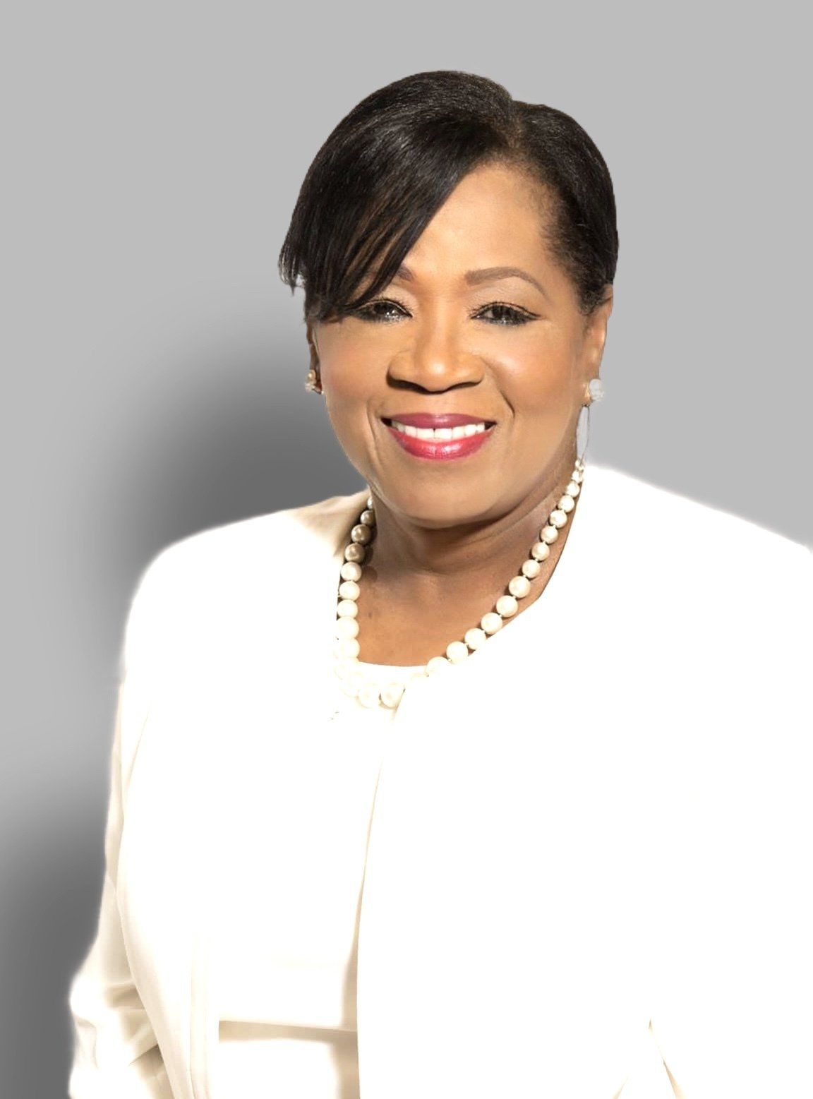 A woman wearing a white jacket and pearls is smiling for the camera.