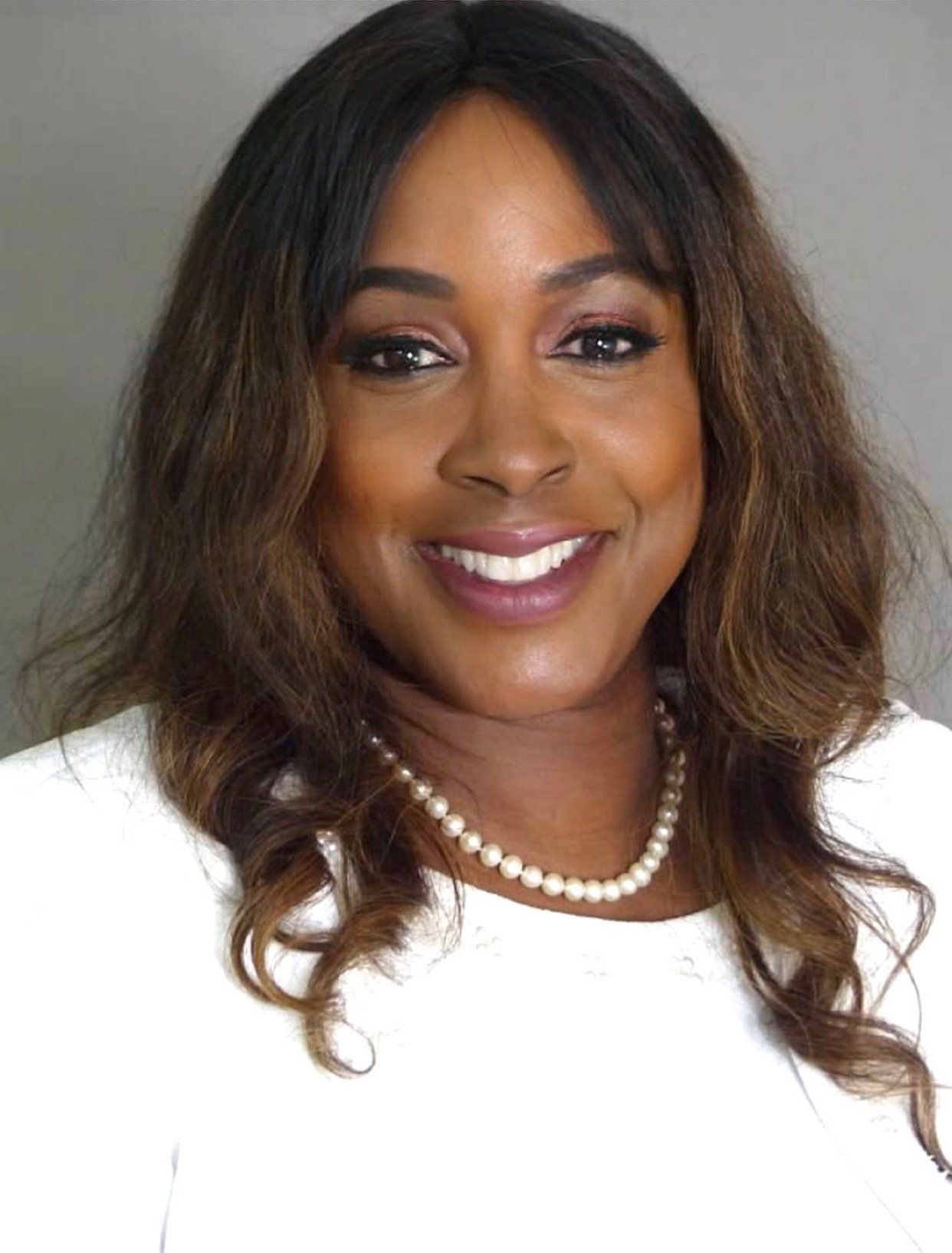 A woman wearing a white shirt and a pearl necklace is smiling for the camera.