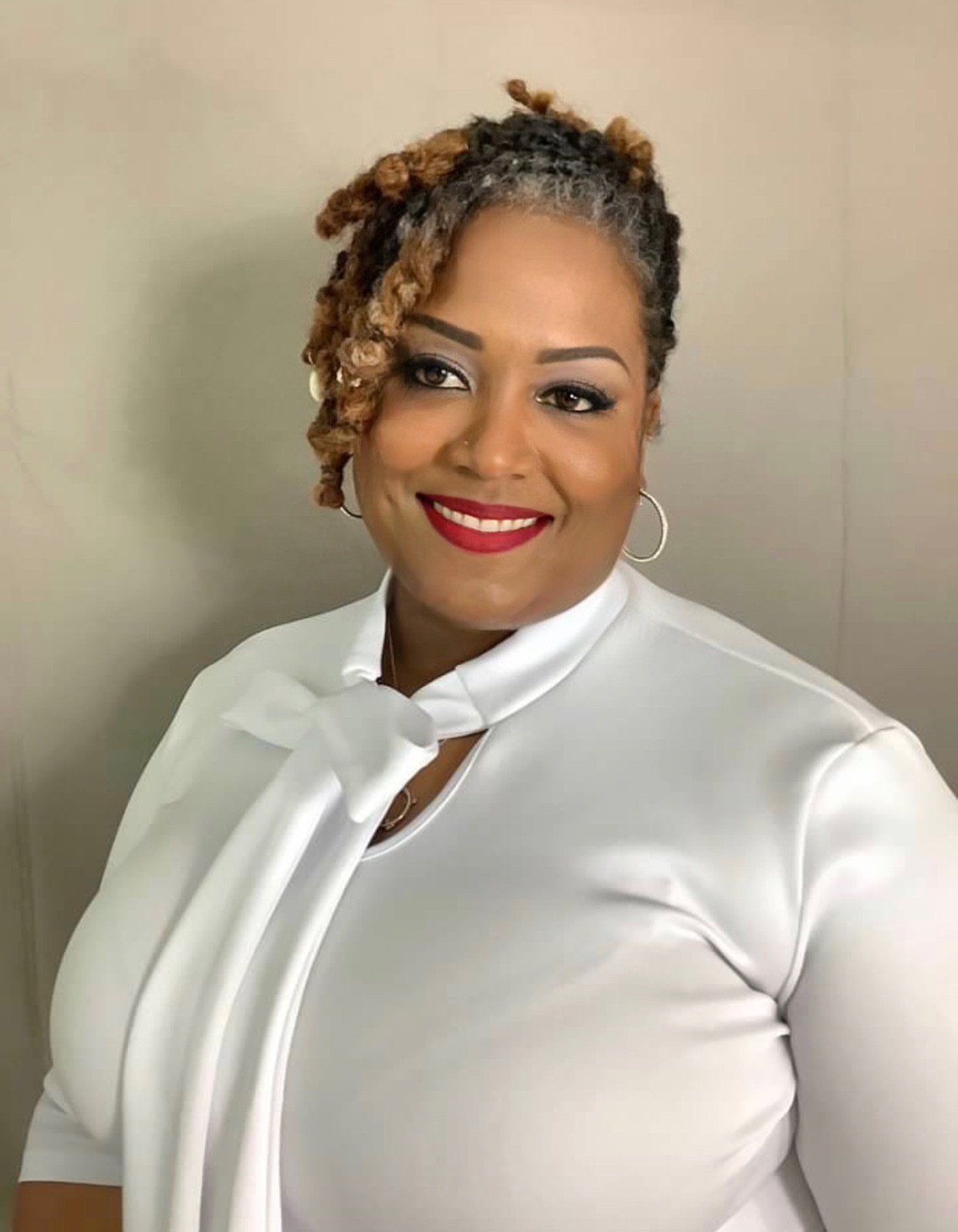 A woman wearing a white shirt and red lipstick is smiling for the camera.