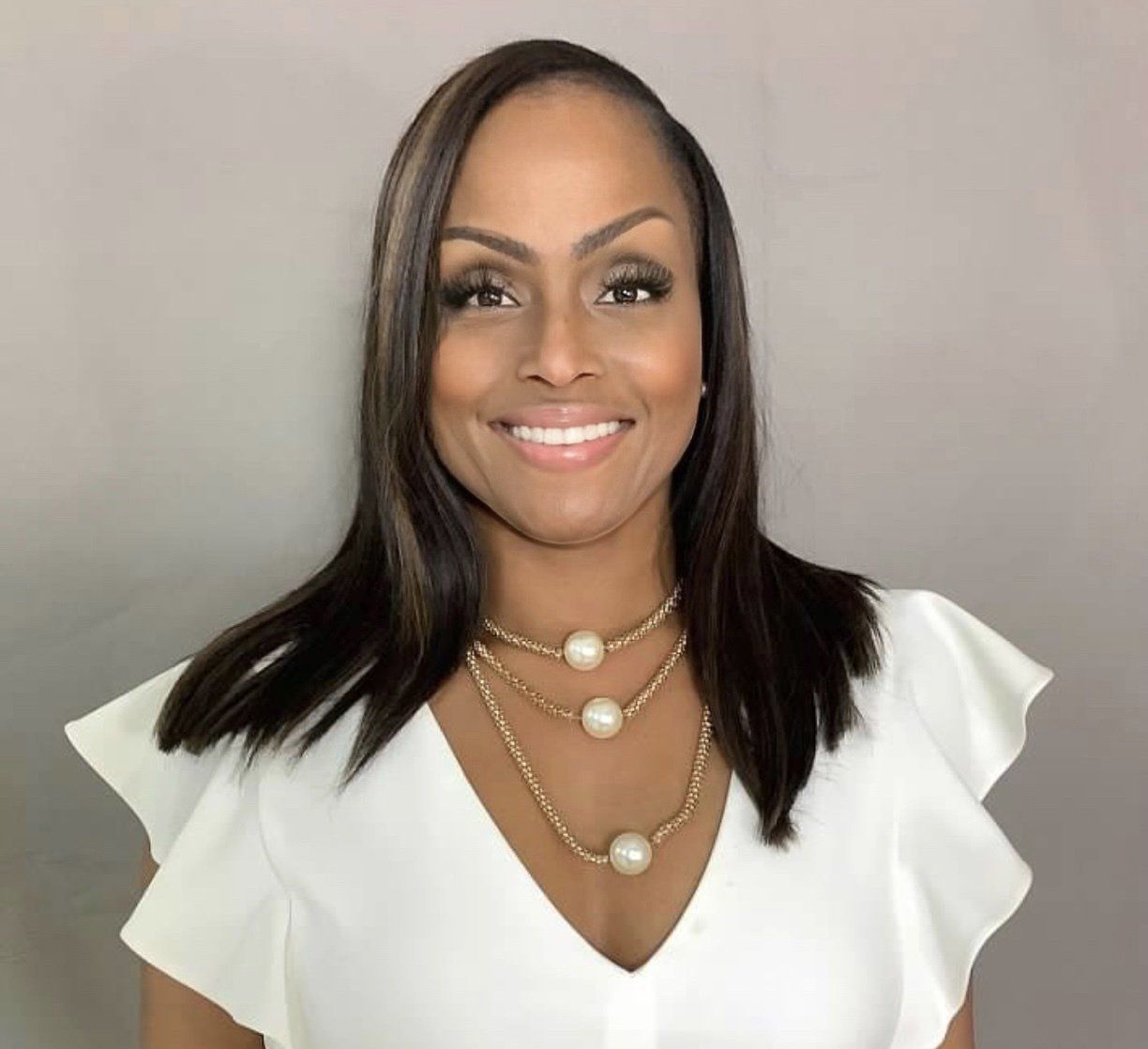 A woman wearing a white shirt and a pearl necklace is smiling for the camera.