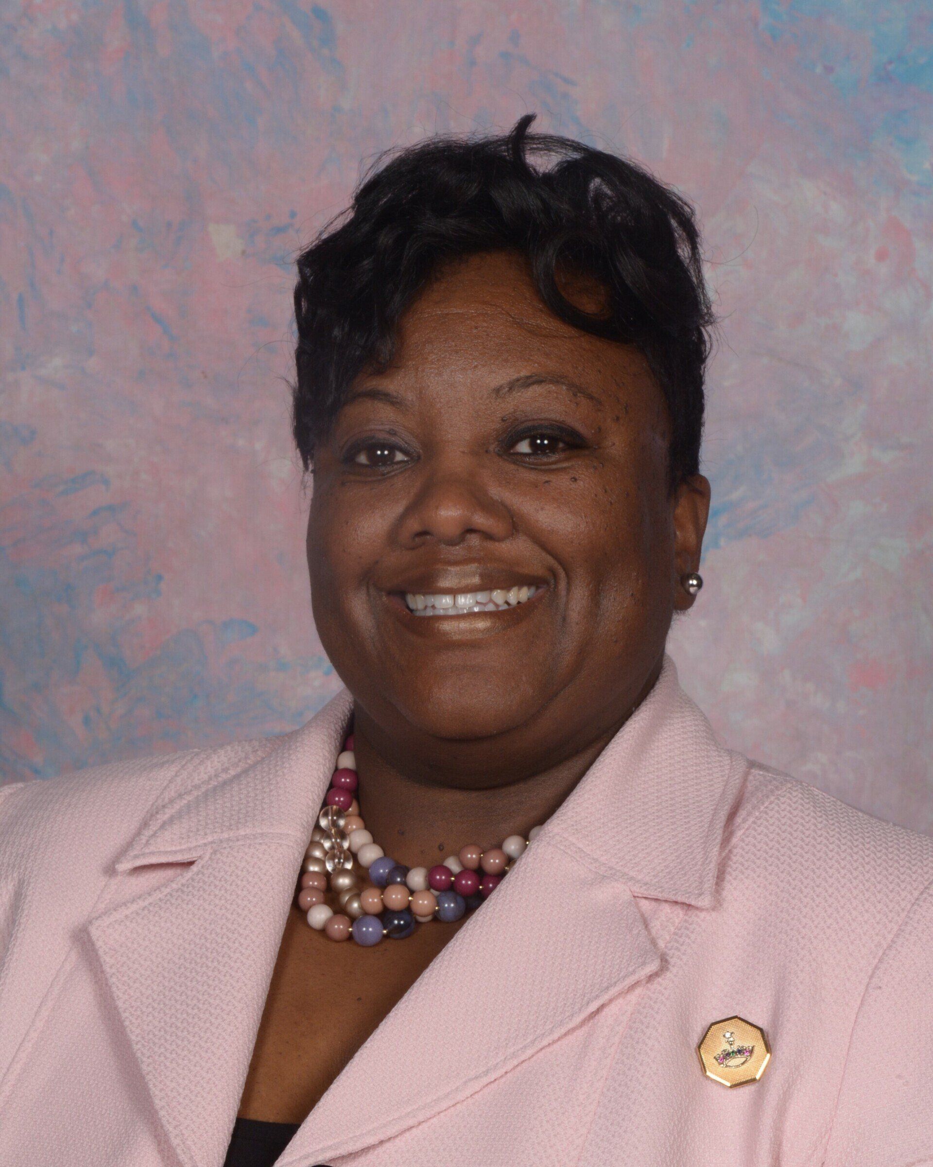 A woman in a pink jacket and necklace is smiling