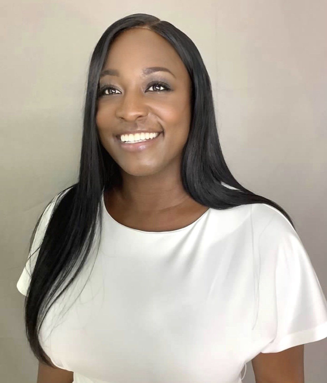 A woman with long black hair is wearing a white shirt and smiling.