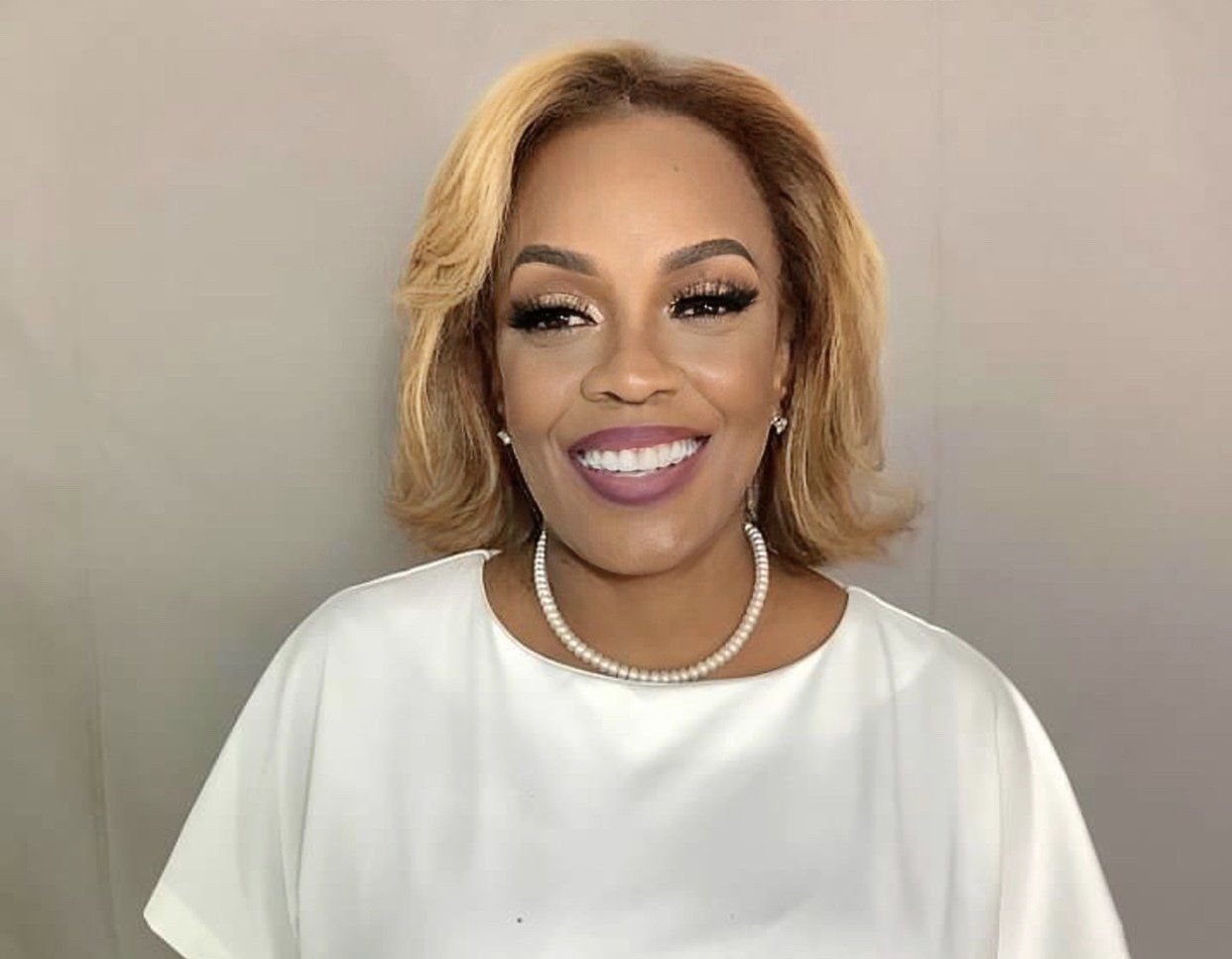 A woman wearing a white shirt and a pearl necklace is smiling.