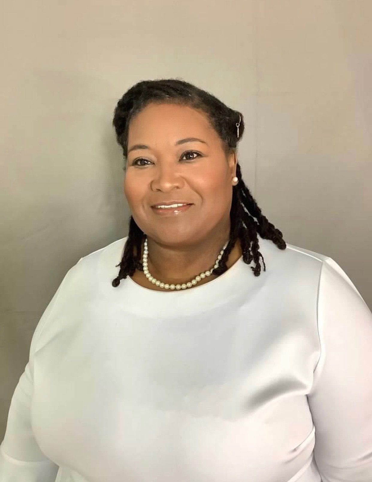 A woman wearing a white shirt and a pearl necklace is smiling for the camera.