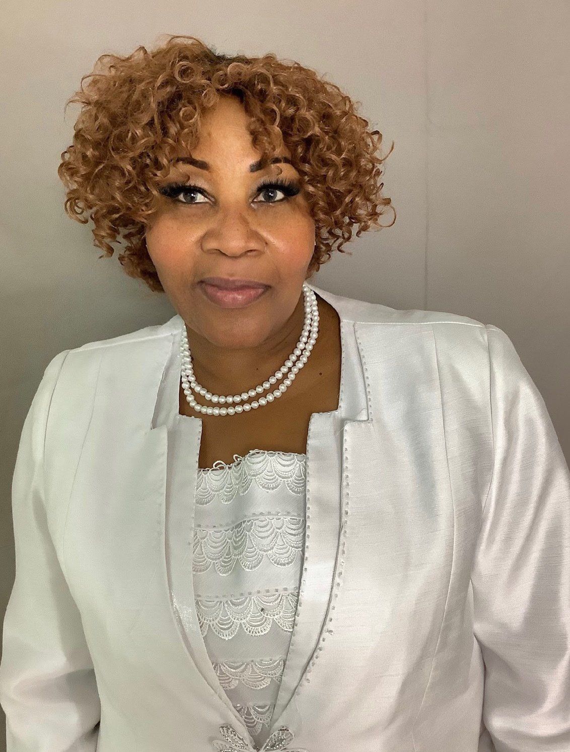 A woman with curly hair wearing a white jacket and pearls