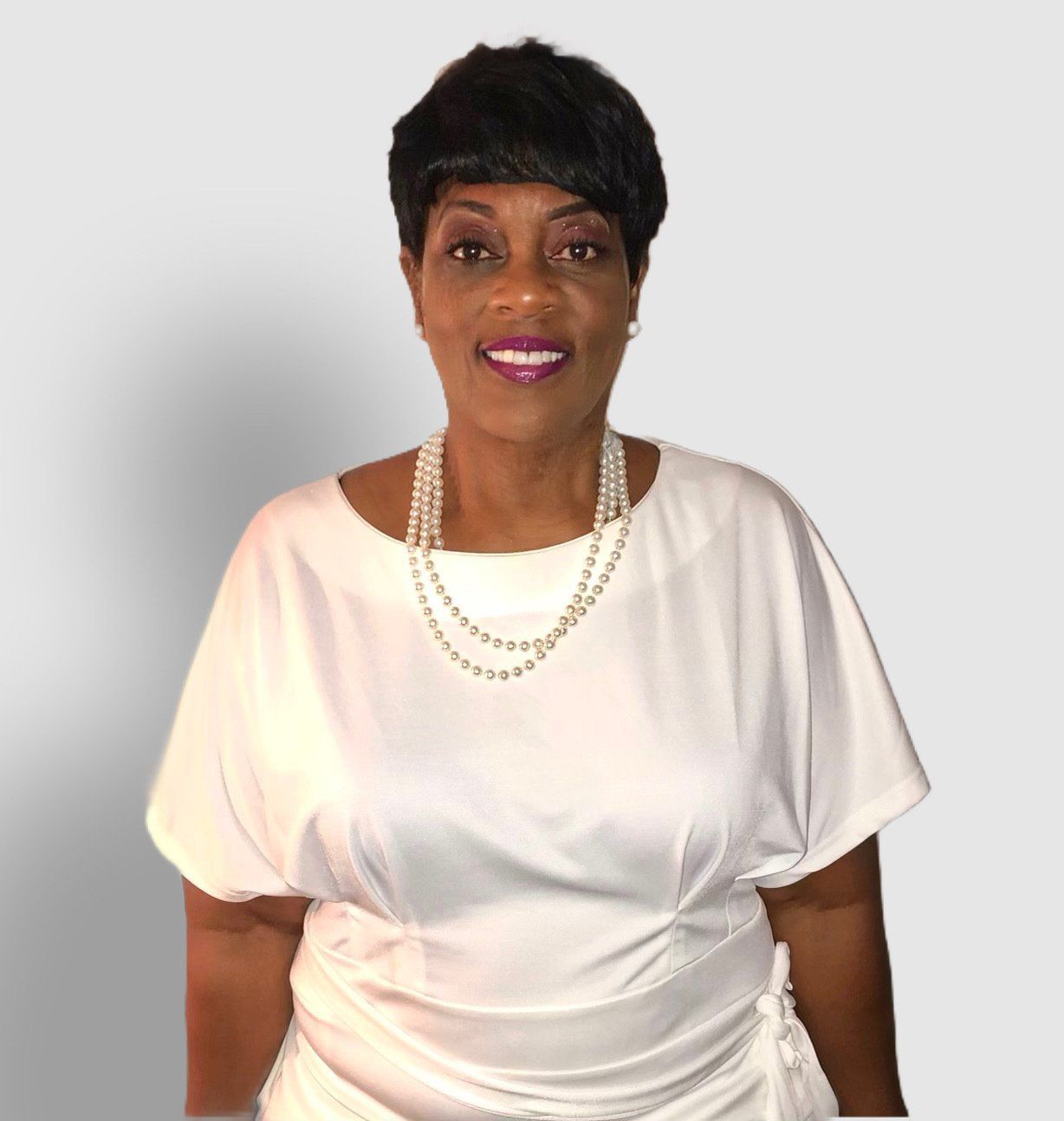 A woman wearing a white top and a pearl necklace is smiling.