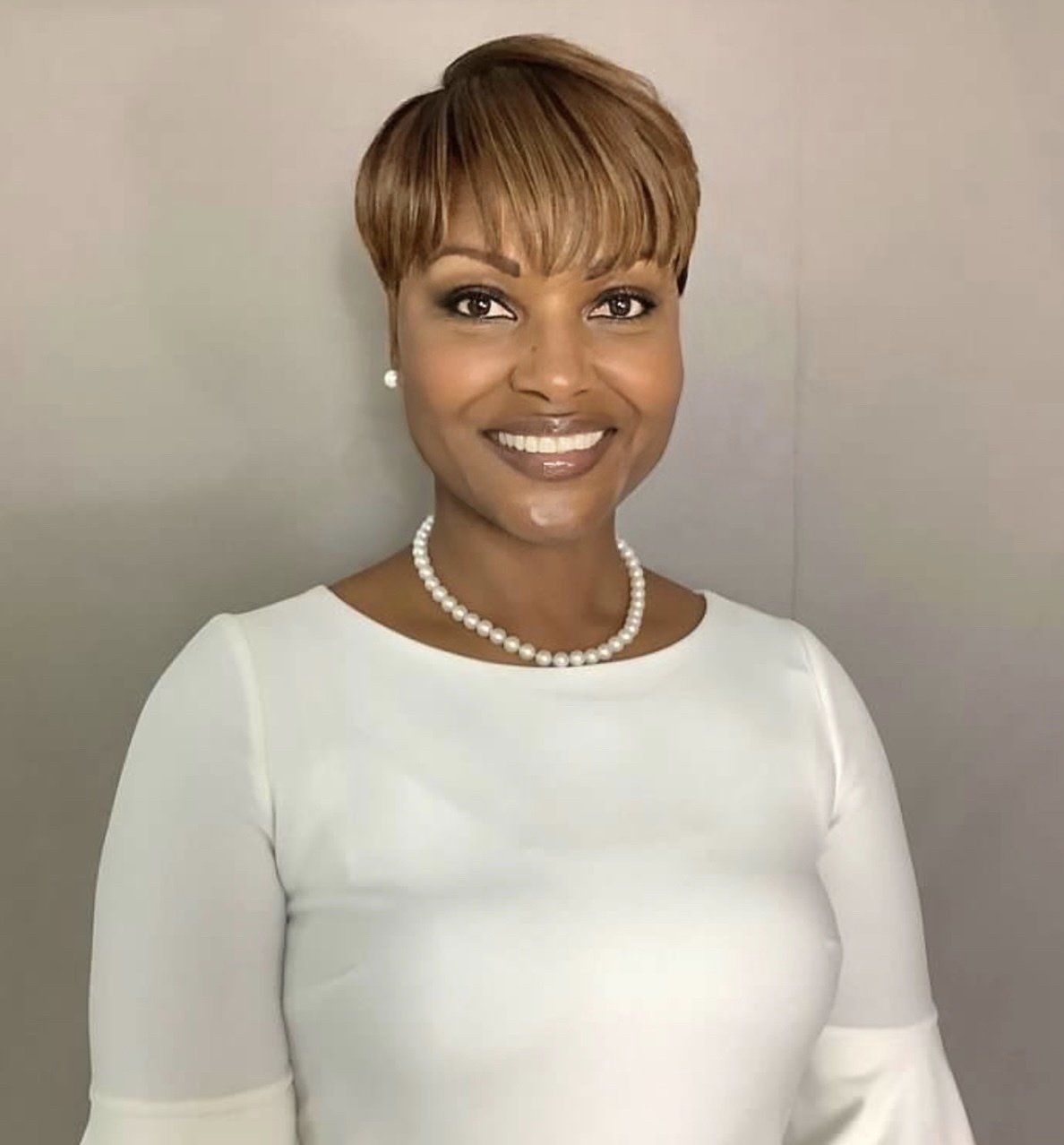 A woman wearing a white shirt and a pearl necklace is smiling for the camera.