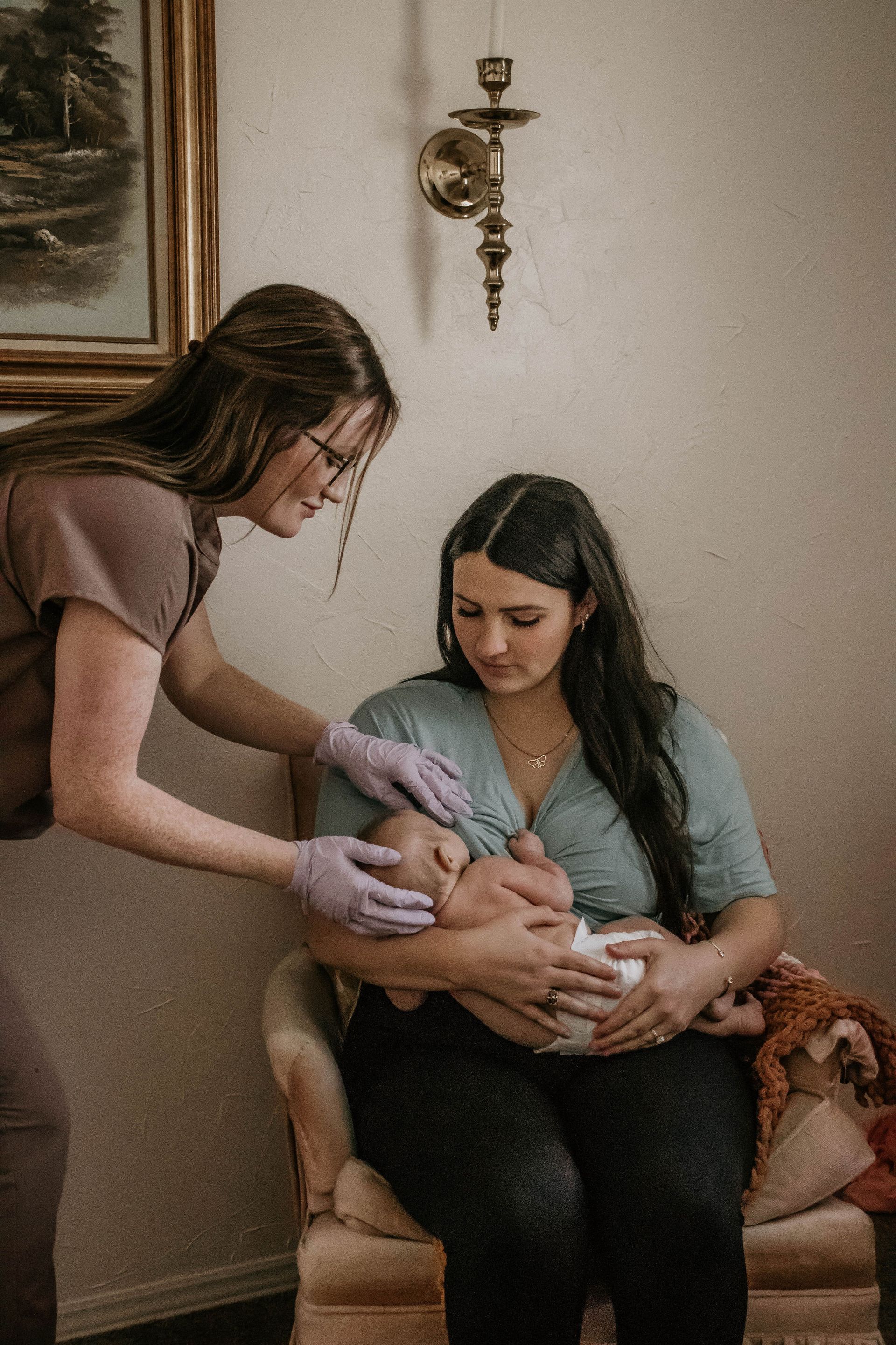 Woman holding baby while another person examines it; indoor setting.