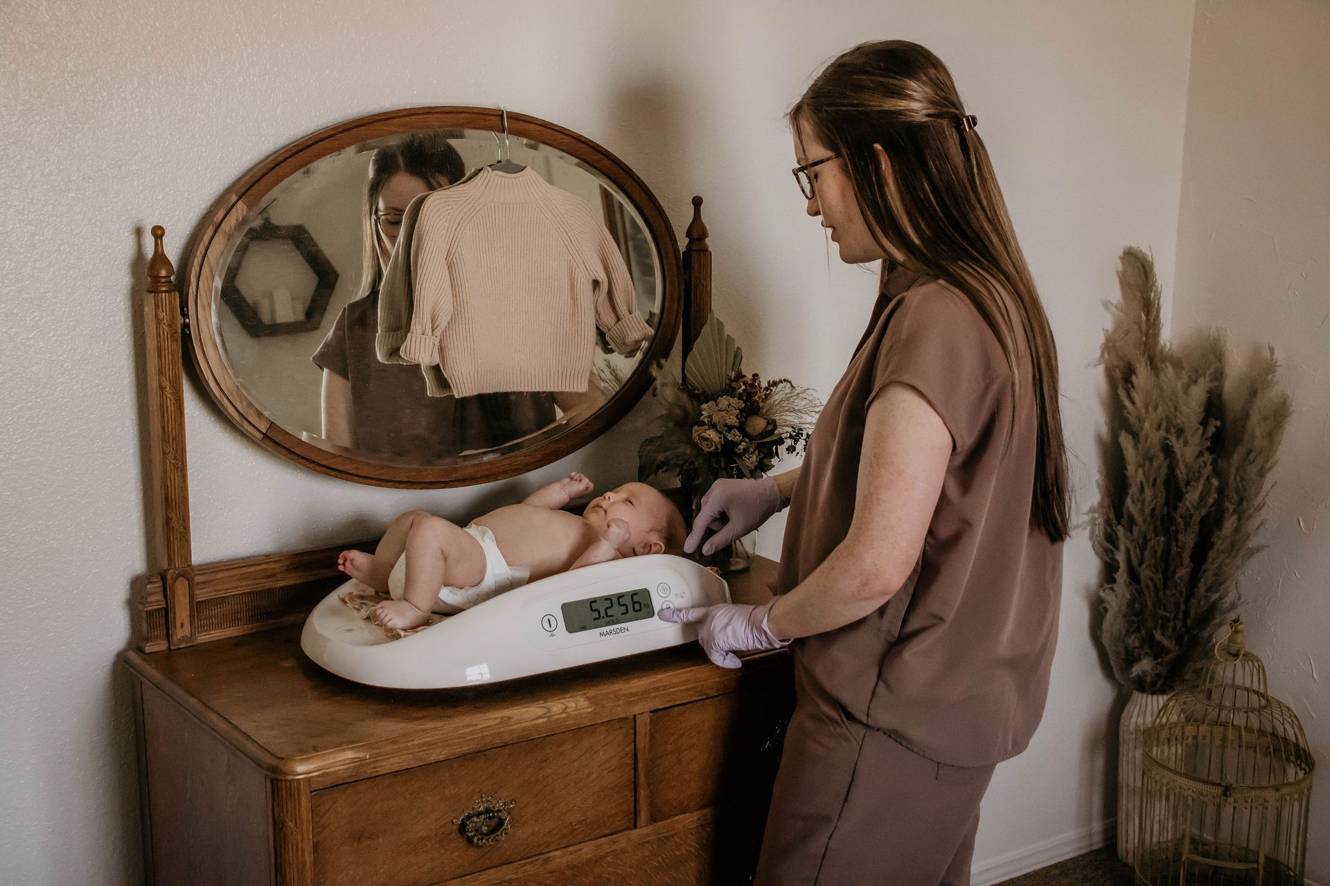 Nurse weighing newborn baby on a digital scale in a room.