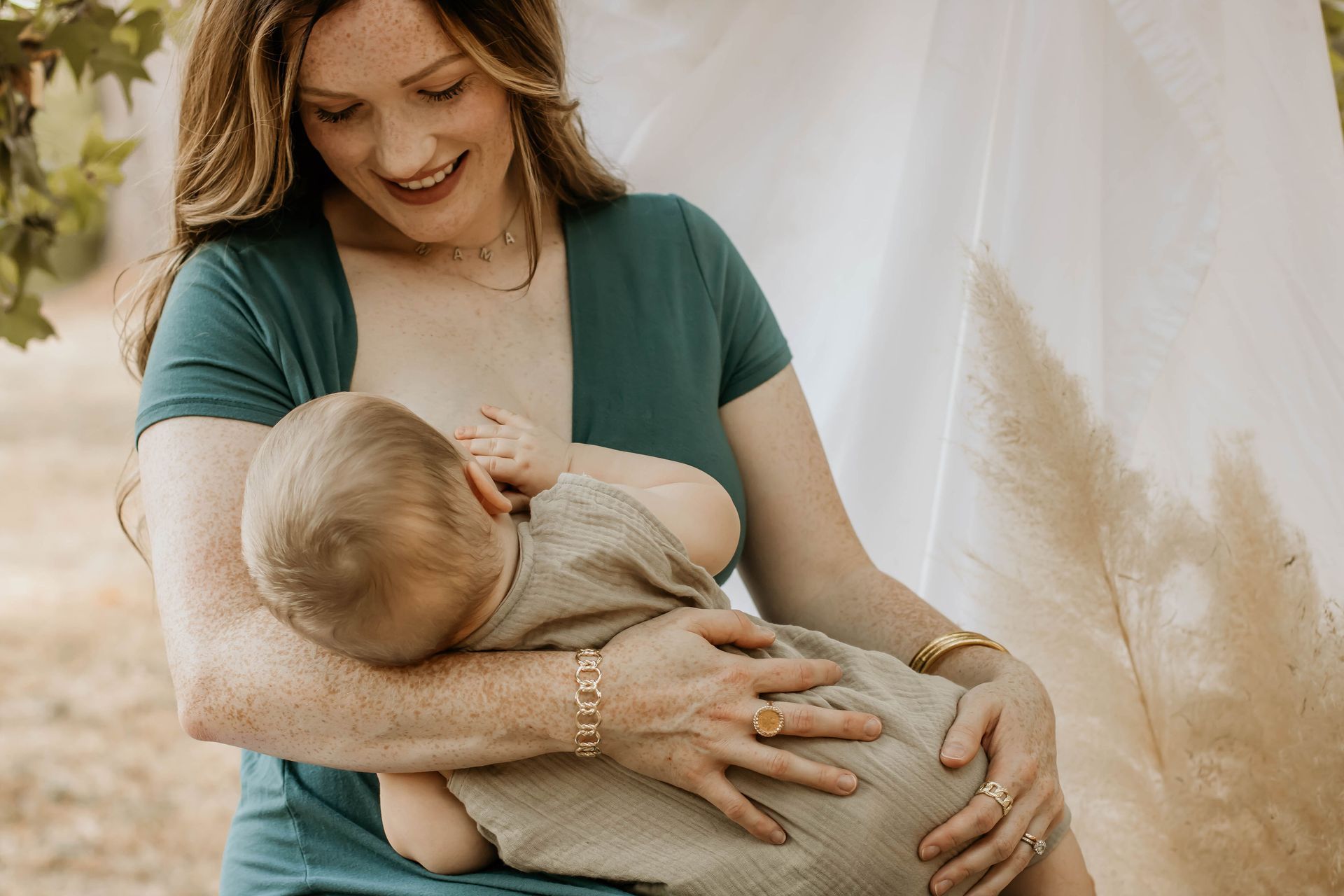 Woman in green top breastfeeding baby outdoors, smiling.