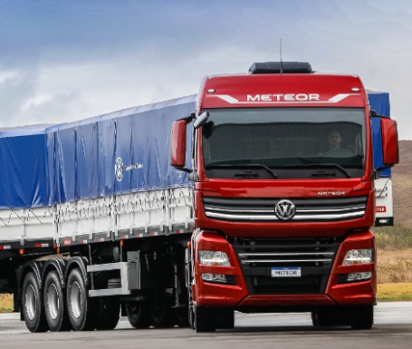 Caminhão vermelho Volkswagen Meteor puxando um trailer de carga com cobertura azul em uma estrada.