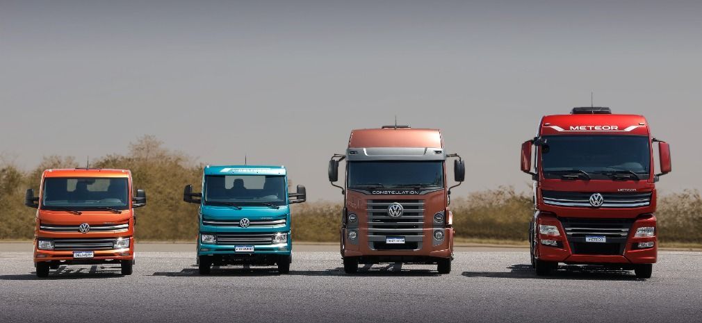 Quatro caminhonetes Volkswagen de tamanhos variados enfileiradas. Nas cores laranja, azul-petróleo, marrom e vermelho.