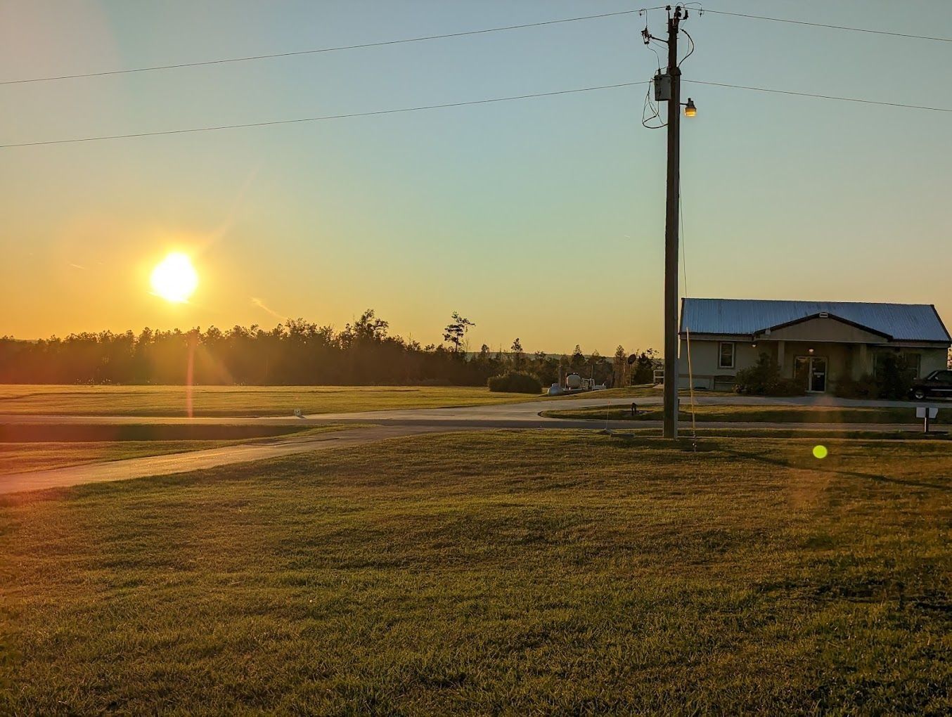 Sunset over a field with a house and utility pole. Golden light, blue sky.