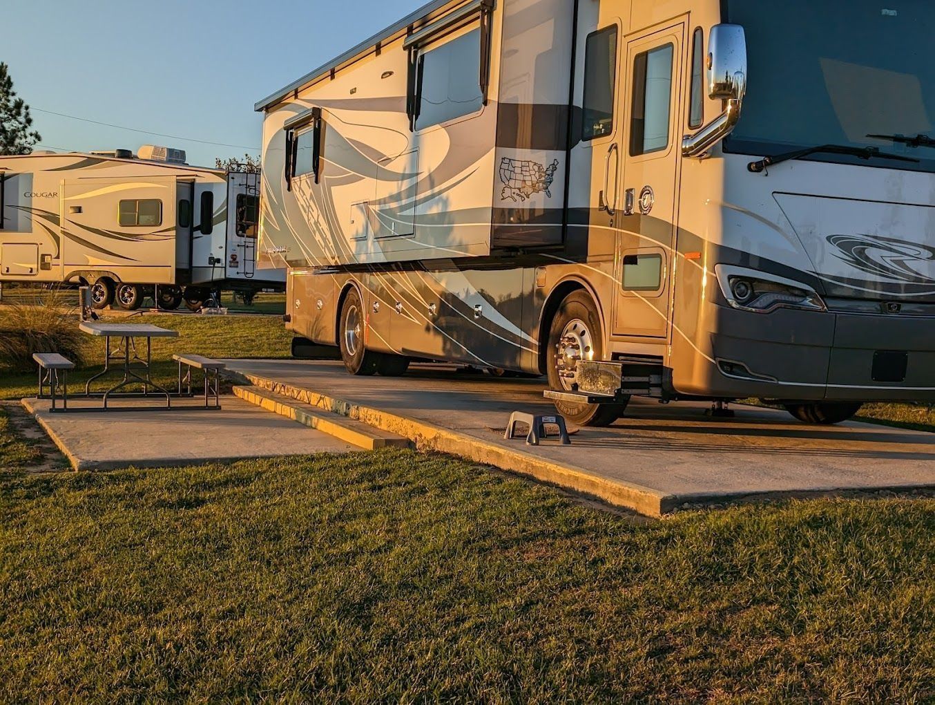 Large RV parked at a campsite with other RVs and a picnic table, grassy area.